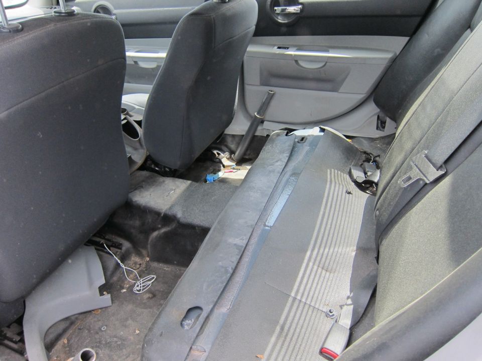 Back seat and interior of a car, showing worn seats and some disarray on the floor