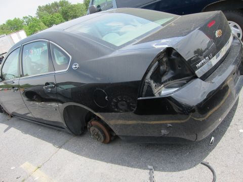 1991 Ford LTD Crown Victoria - Rear view of a black sedan with a missing wheel and dented bumper.