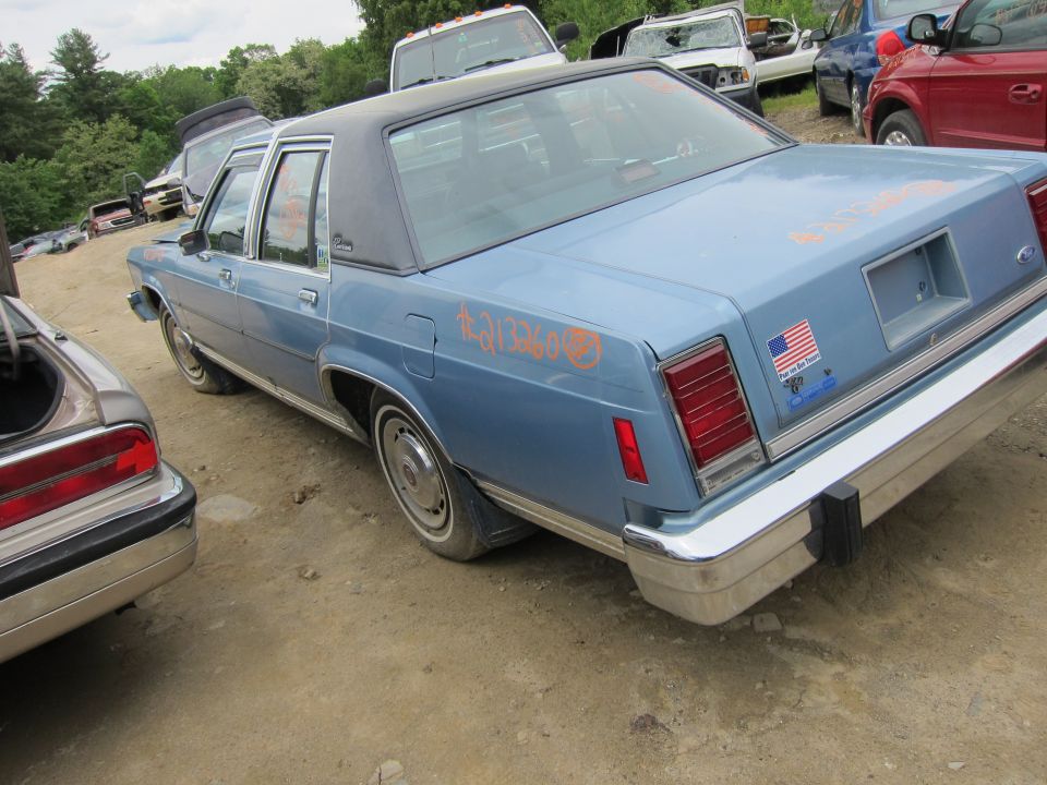 Blue sedan with a black vinyl roof, seen from the rear quarter. Orange graffiti is on the rear fender. An American flag sticker is on the trunk lid