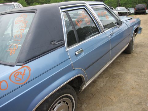 2001 Ford Crown Victoria - A blue sedan, possibly an older model Crown Victoria, is seen from the side in an outdoor lot with other vehicles.