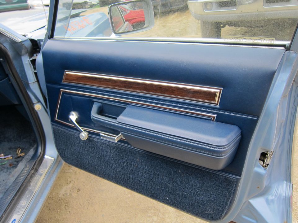 Blue interior door panel with wood trim, armrest, and window crank