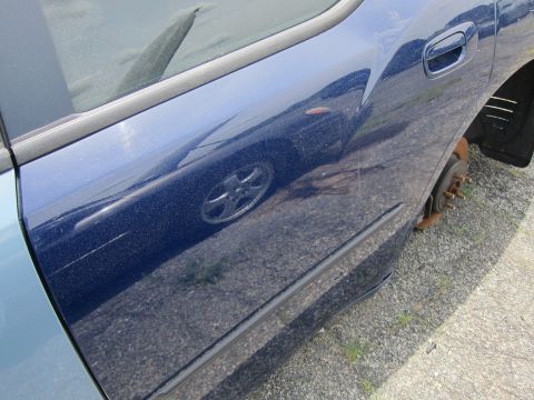 1991 Ford LTD Crown Victoria - Side view of a blue car with a missing wheel, reflecting another vehicle in its paint.