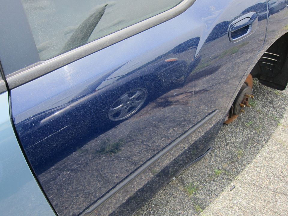 Close-up of a blue car's side door and fender, showing a missing wheel and reflection of another car