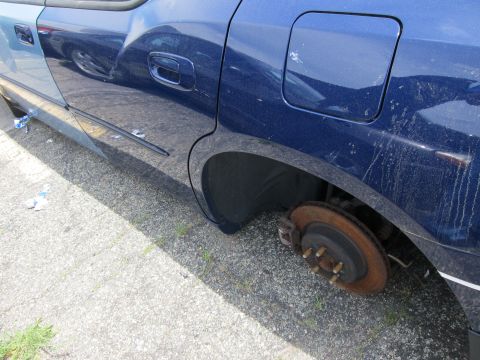 1991 Ford LTD Crown Victoria - The rear wheel of a blue sedan has been removed, exposing the brake assembly and lug studs.