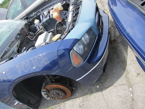 1991 Ford LTD Crown Victoria - A damaged blue police car sits in a lot with its hood open and one front wheel missing.