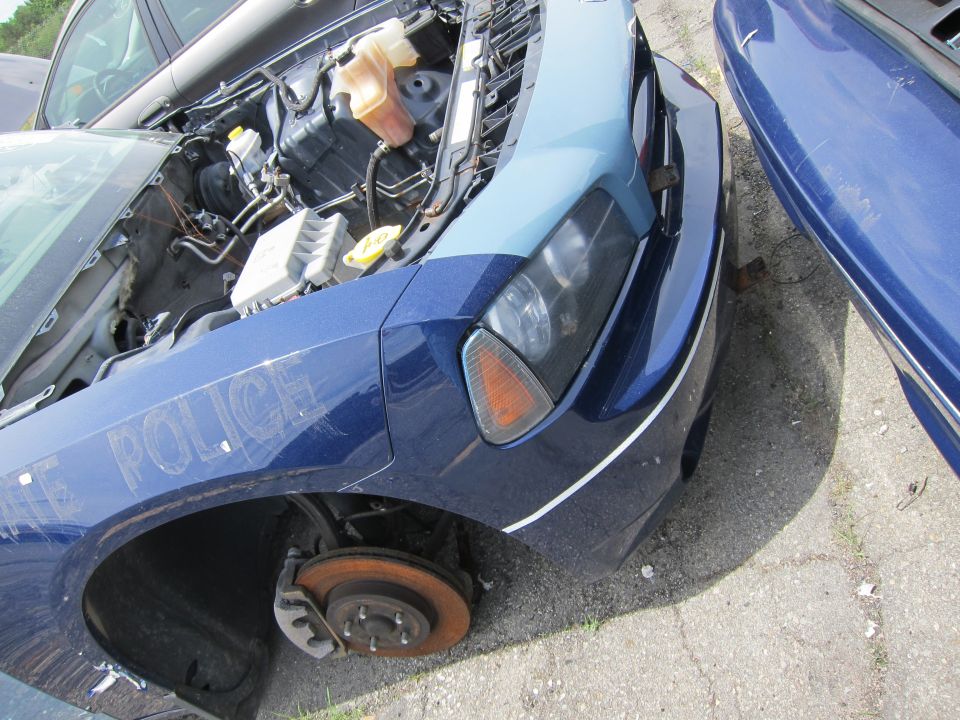 Blue police car with hood open, missing front wheel, and "POLICE" text on fender