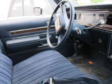 2001 Ford Crown Victoria - The interior of a car shows blue fabric seats, wood grain trim, and a steering wheel with a diamond-shaped emblem.