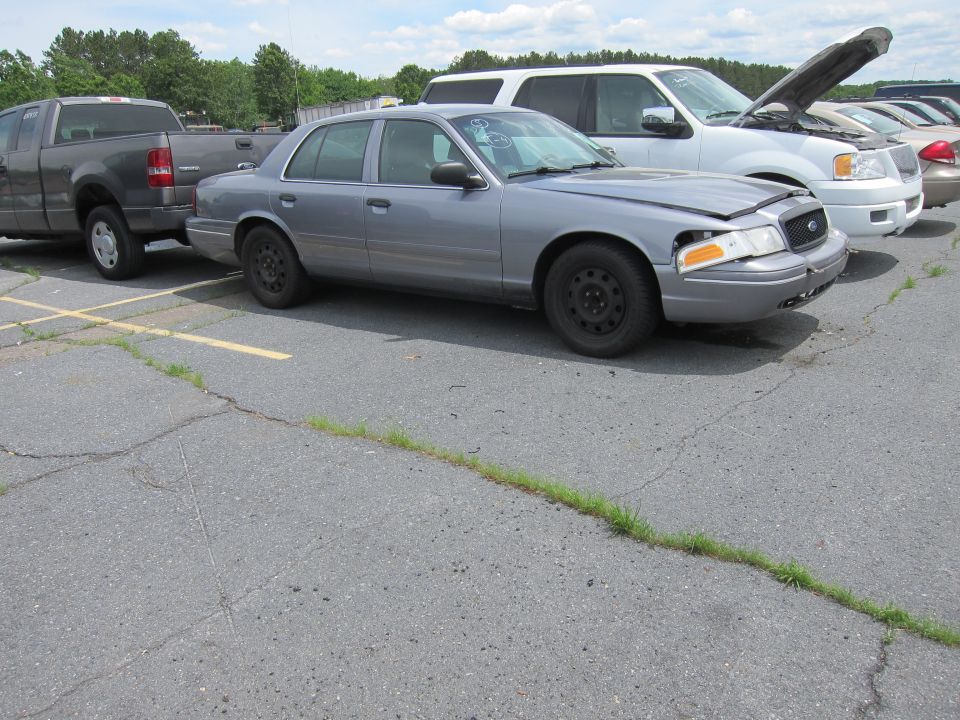 Gray Ford Crown Victoria sedan parked on cracked asphalt, front passenger side damaged