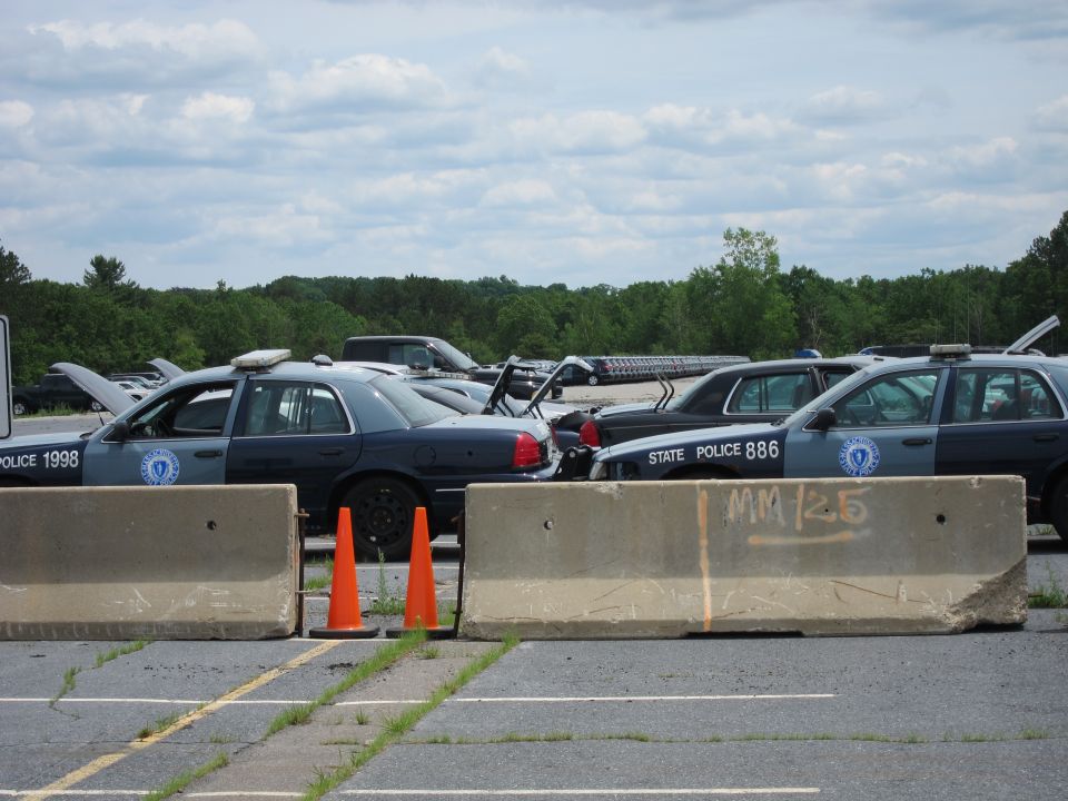 Several police cars parked behind concrete barriers, one marked 'POLICE 1998'