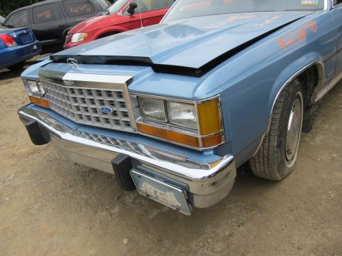 2001 Ford Crown Victoria - The front grille and headlights of a blue sedan are visible, with other cars in the background.
