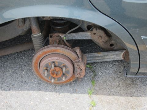 1991 Ford LTD Crown Victoria - Close-up of a car's heavily rusted rear brake and suspension system, showing significant wear and tear.