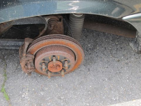 1991 Ford LTD Crown Victoria - Close-up view of the rear brake rotor and suspension system of a dark-colored vehicle.