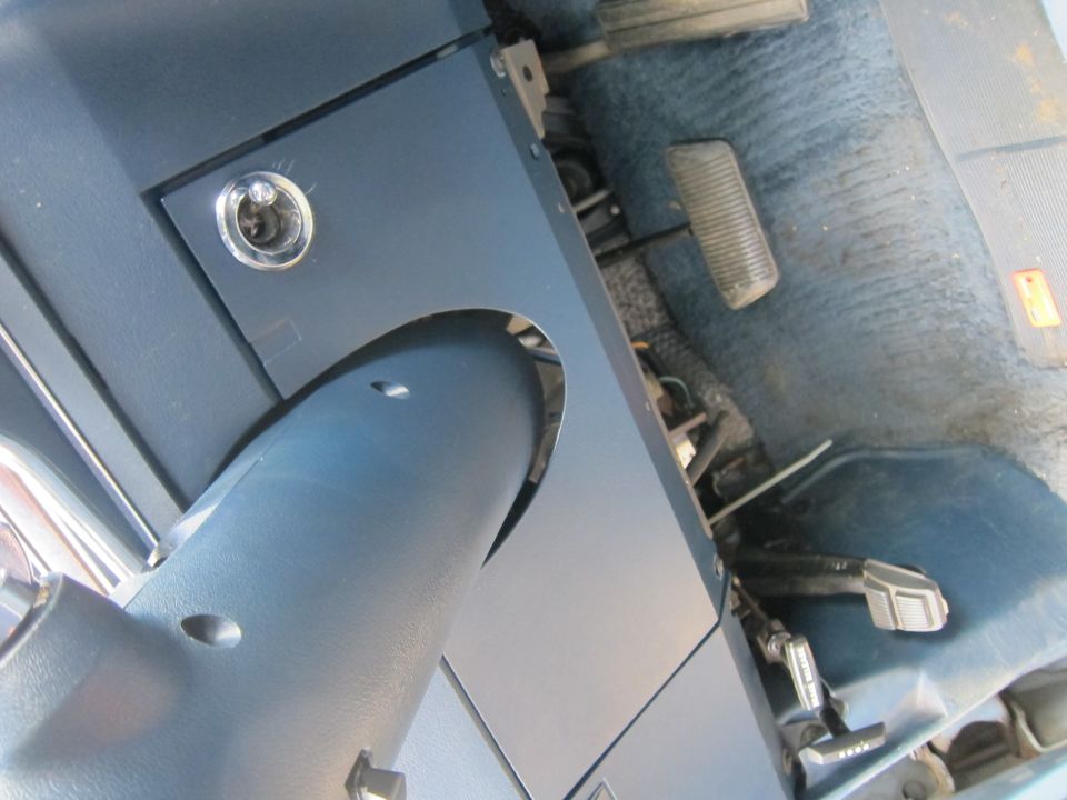 Close-up of blue interior with steering column, pedals, and floor mat