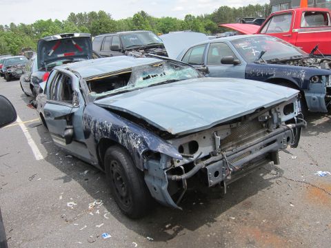 1991 Ford LTD Crown Victoria - Damaged police car with missing front end and shattered windshield sits in a junkyard lot.