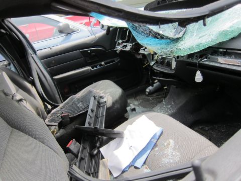 1991 Ford LTD Crown Victoria - The interior of a car shows significant damage, including a shattered windshield and torn upholstery, with another vehicle visible through…