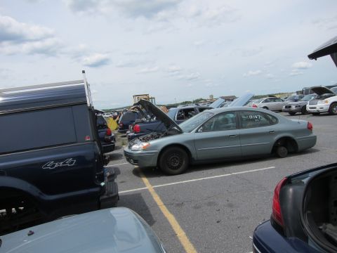 1991 Ford LTD Crown Victoria - A junkyard scene with multiple vehicles, including a sedan with its hood open and a missing front wheel.