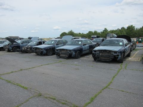 1991 Ford LTD Crown Victoria - A row of damaged Ford Crown Victorias sit in a salvage yard, awaiting parts or disposal.