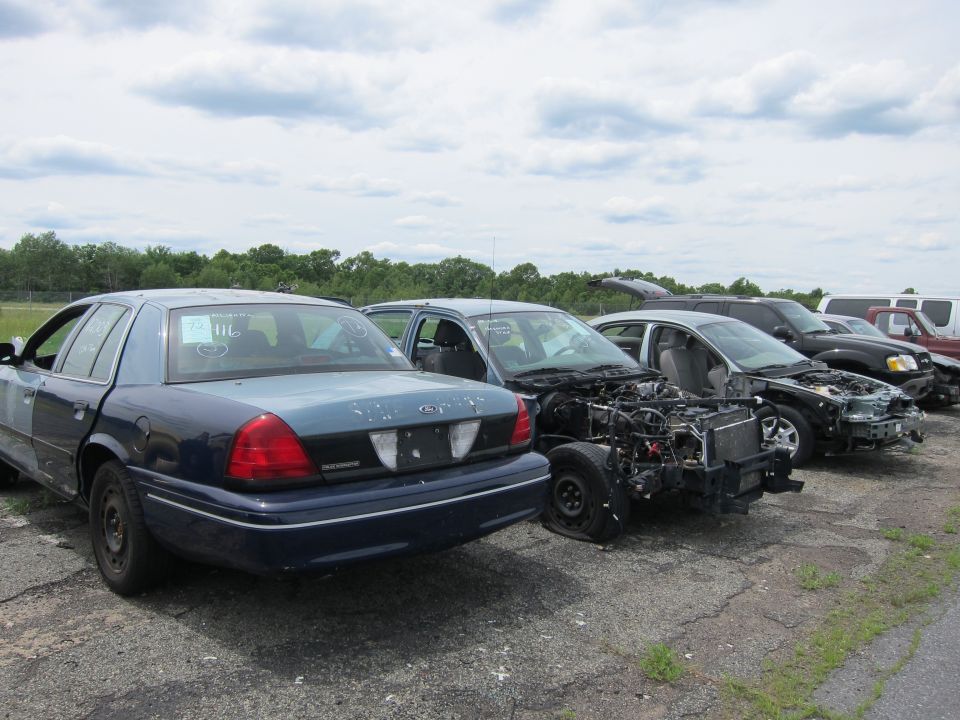 Several cars parked in a lot, some stripped down. The closest car is a blue sedan