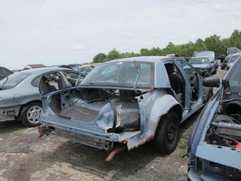 1991 Ford LTD Crown Victoria - A stripped-down sedan sits in a junkyard, showing extensive rust and missing parts.