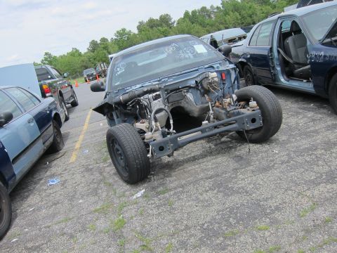 1991 Ford LTD Crown Victoria - The front end of a blue car, stripped of its engine and front body panels, sits in a junkyard with other vehicles visible.