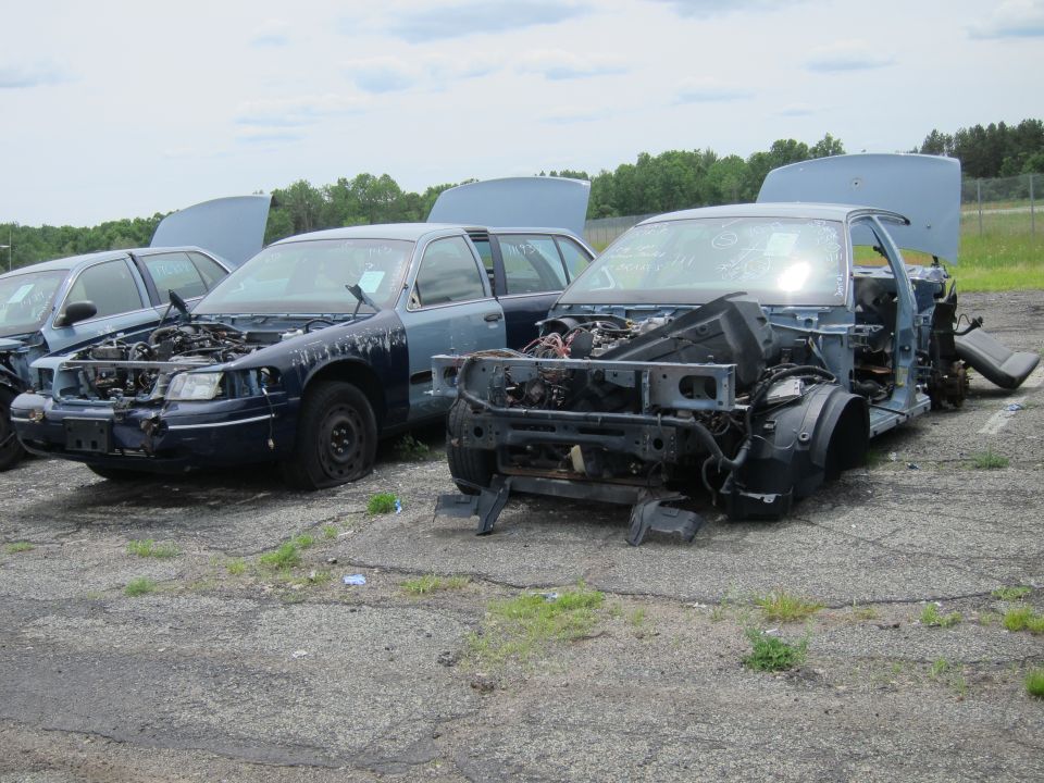 Two wrecked blue sedans with hoods open, one missing its front end