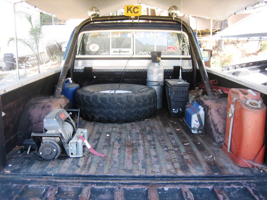 Pickup truck bed loaded with a spare tire, winch, gas cans, and a propane tank