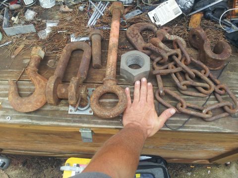 1988 Ford Bronco - A collection of large, rusty metal hardware, including tow hooks, shackles, and chain, is laid out on a wooden surface.