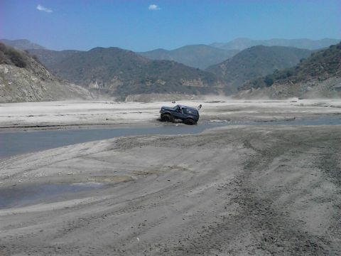 1988 Ford Bronco - SUV driving through a dry riverbed with water and mud.