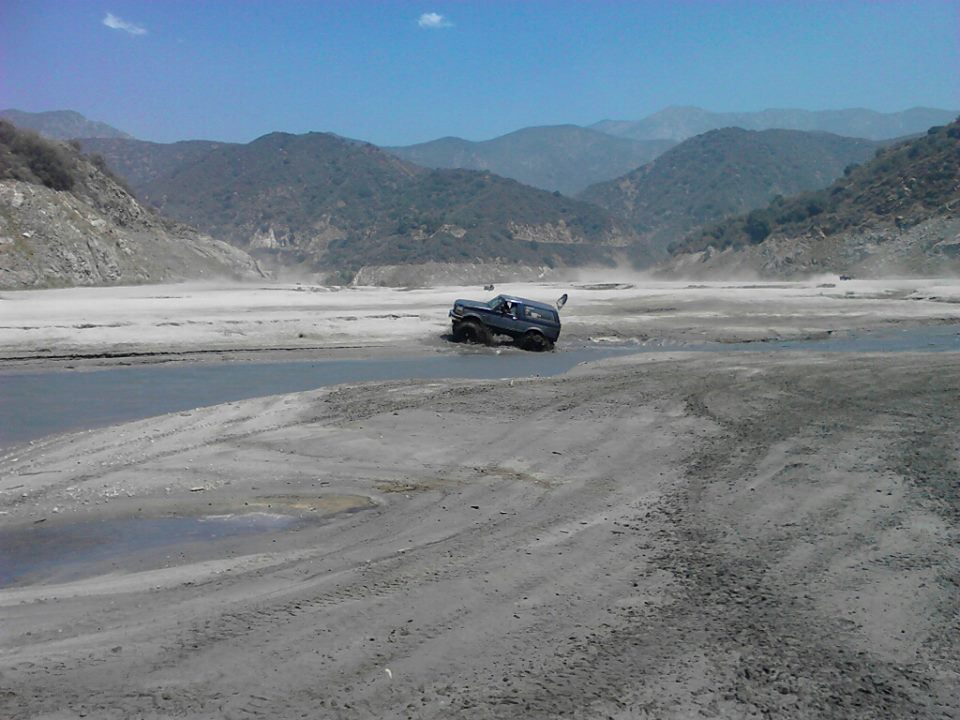 dark SUV navigating a muddy, watery terrain with mountains in the background