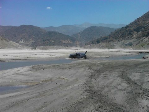 1988 Ford Bronco - A vehicle navigates through a dusty, water-filled terrain with hills in the background.