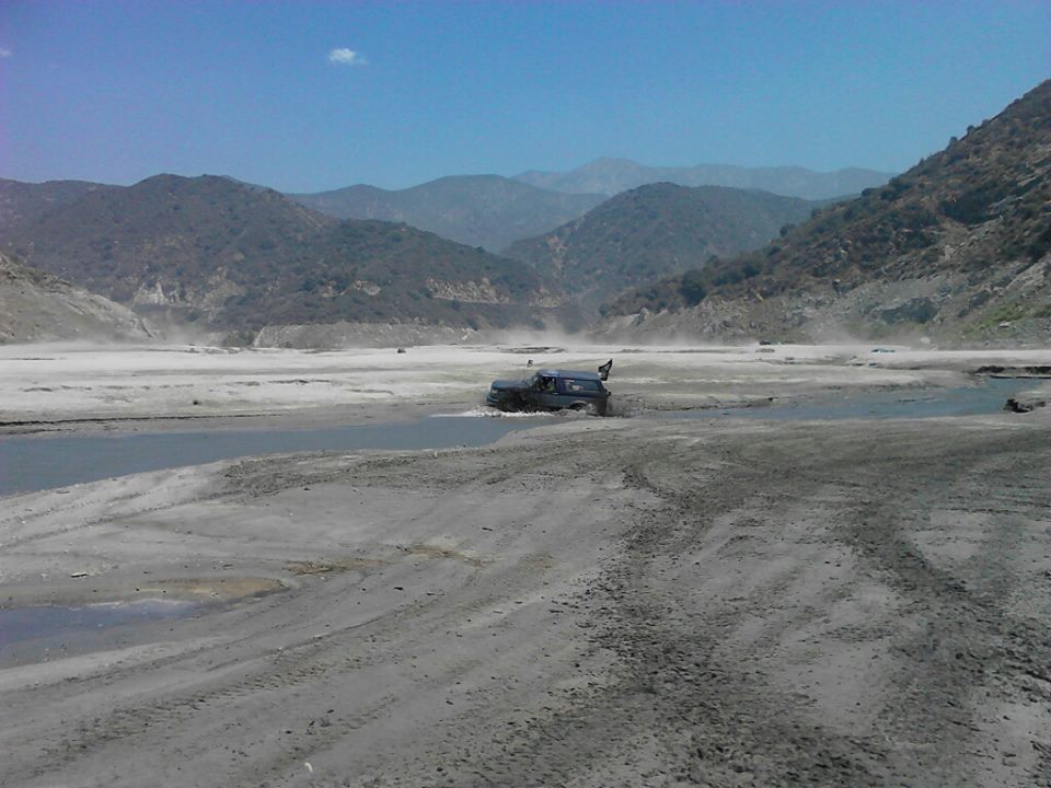 SUV driving through shallow water in a dry, mountainous area. Some dust is kicked up