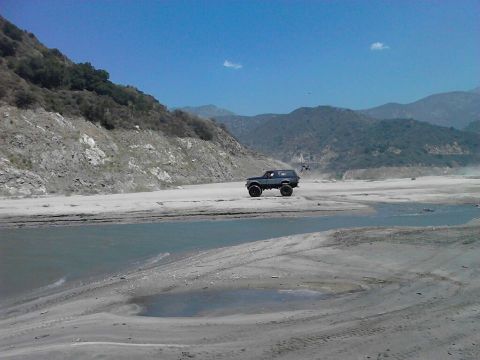1988 Ford Bronco - A dark blue SUV navigates a dry riverbed with mountains in the background.