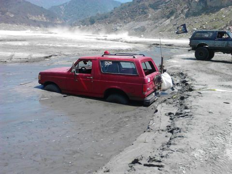 1988 Ford Bronco - A red 1987 Ford Bronco is stuck in thick mud, with another off-road vehicle visible in the background.