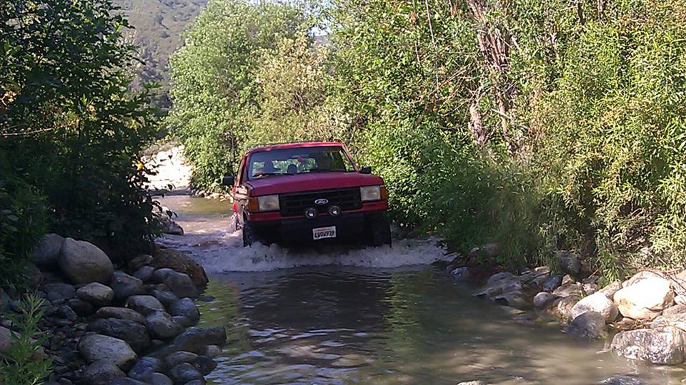 Red 1992 Ford Bronco driving through a stream
