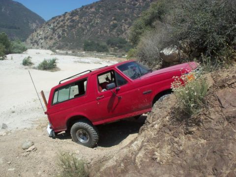 1988 Ford Bronco - A red Ford Bronco navigates a challenging rocky path with a flat tire.
