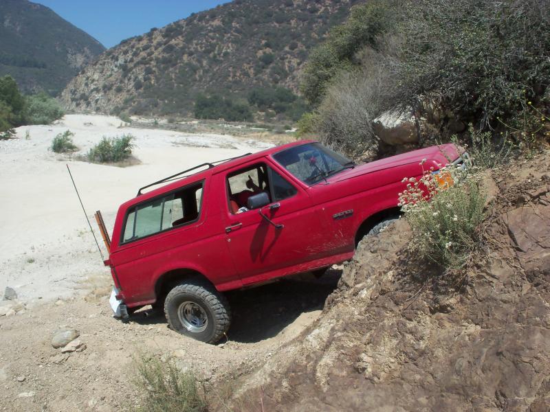 Red Ford Bronco with flat tire stuck on rocky terrain