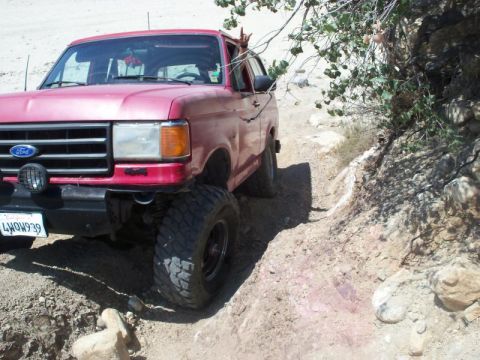 1988 Ford Bronco - This red Ford Bronco is navigating a challenging off-road path with rocky terrain.