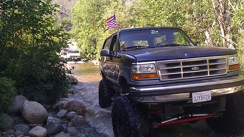 Dark blue SUV with lifted suspension driving through a stream, California license plate 3JYB028