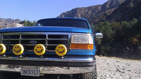 1988 Ford Bronco - Blue Ford truck with smiley face lights parked outdoors with mountains in the background.