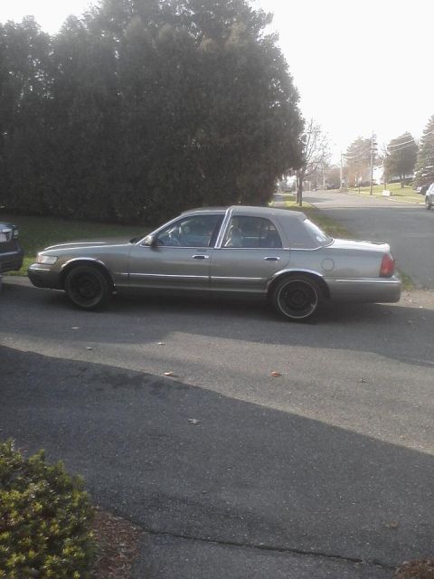 2001 Mercury Grand Marquis - A gray sedan is parked on a street with trees and houses in the background.
