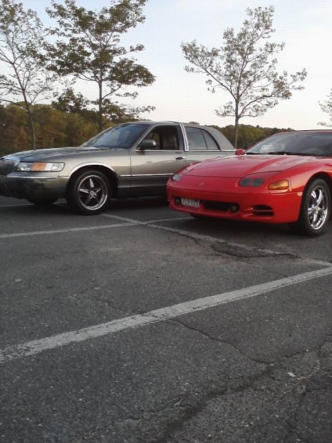 2001 Mercury Grand Marquis - A silver sedan and a red sports car are parked side-by-side in a parking lot.