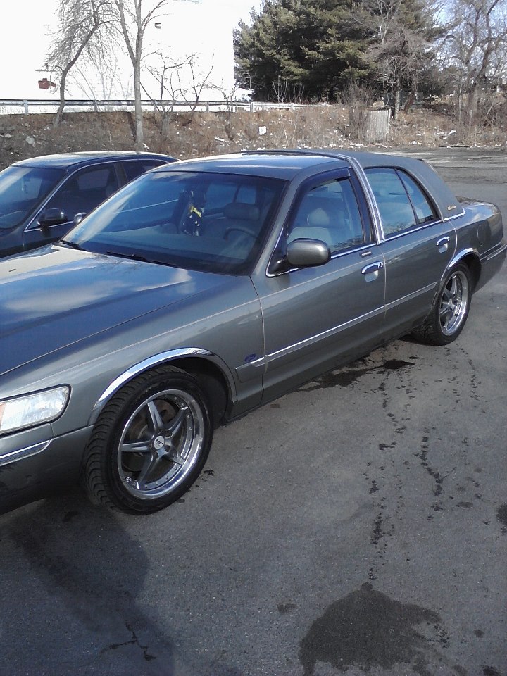 1998 Mercury Grand Marquis sedan, gray, with aftermarket wheels. Another car is parked behind it