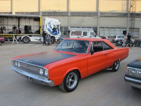1991 Ford Crown Victoria - This orange 1967 Dodge Coronet coupe has a black hood and custom wheels, seen at an outdoor event with other vehicles and a stage.
