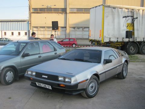 1991 Ford Crown Victoria - A DeLorean DMC-12 is parked next to another car, with a large truck in the background.