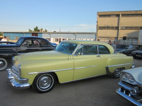 1991 Ford Crown Victoria - A pale yellow 1950s coupe is parked outdoors with several other vehicles.