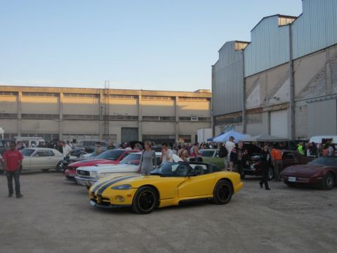 1991 Ford Crown Victoria - A gathering of cars and people outside a large warehouse under a clear sky.