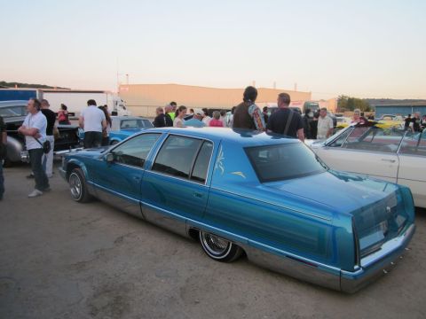 1991 Ford Crown Victoria - A customized blue sedan is parked at an outdoor gathering with several people visible.