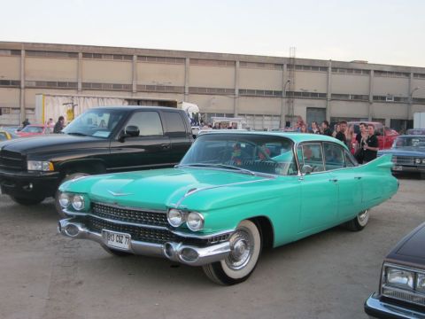 1991 Ford Crown Victoria - A teal 1959 Cadillac sedan is parked next to a black pickup truck, with a crowd gathered in the background.