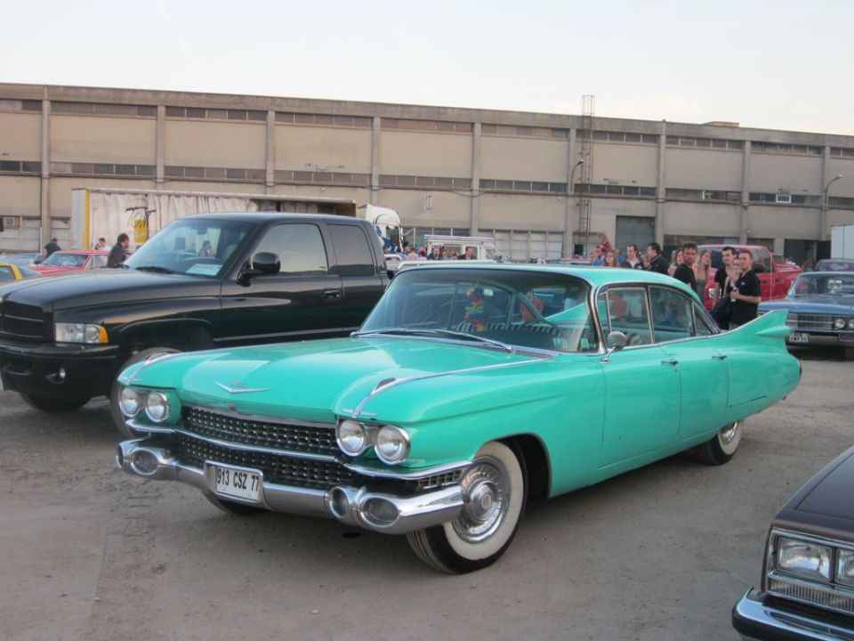 Teal 1959 Cadillac sedan with prominent tail fins, front 3/4 view