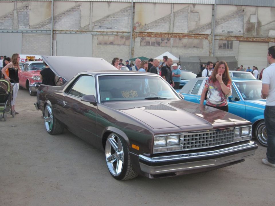 Brown 1980s Chevrolet El Camino with chrome wheels, hood open, parked at an outdoor car show